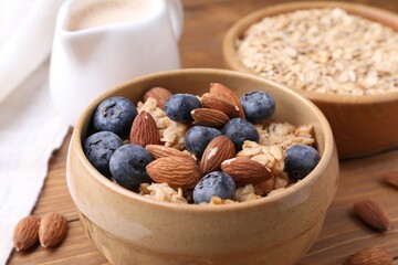 Oat flakes, almond milk, nuts and blueberries on wooden table, closeup