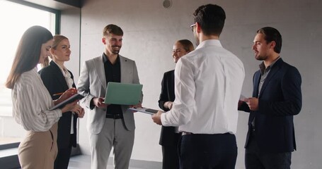 Group of company employees standing with laptops and notepads, discussing ideas, brainstorming, working on collaborative project together. Team of professionals having conversation about work issues. - Powered by Adobe