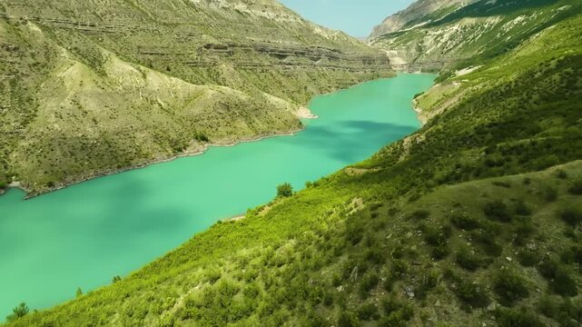 Aerial footage of the picturesque Sulak Canyon in the Caucasus Mountains, Dagestan, Russia. Features the vibrant turquoise river and lush green mountainsides on a sunny summer day, a major natural lan