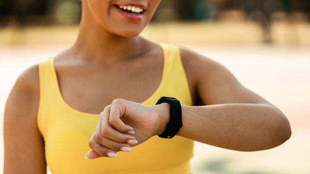 Closeup cropped view of smiling African American lady using smartwatch to monitor progress. Female athlete checking her performance and running trail looking on wearable fitness wristwatch device - Powered by Adobe