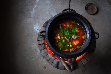 Clay pot cooking on traditional stove with vibrant soup, fresh herbs, and vegetables creates rustic and authentic atmosphere for homemade meals