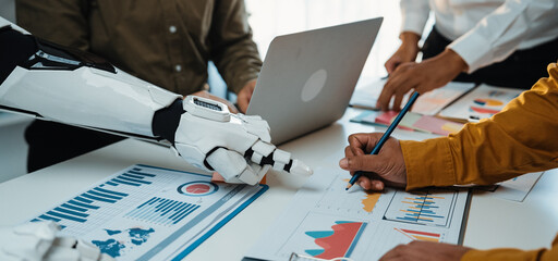 A unique interaction between human and robotic hand in a modern office as they analyze charts and...