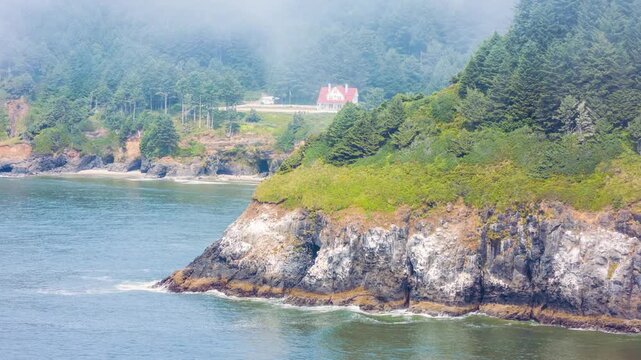A wide shot of the iconic Heceta Head Lighthouse Keeper's House perched on a cliffside overlooking the Pacific Ocean. The scene captures the dramatic, rugged beauty of the central Oregon coast with lu