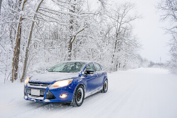 Snow Covered Blue Car On Side of the Road In Winter During a Snowstorm, Dangerous Icy Slippery Winter Driving Road Conditions
