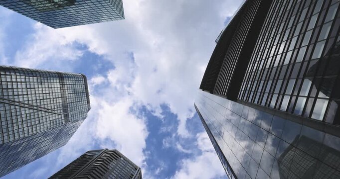 Low-angle view between modern skyscrapers in Frankfurt am Main, looking up at glass and steel office towers against a cloudy blue sky. Contemporary urban architecture in the financial district, convey