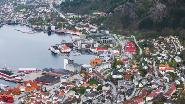 dense coastal town orange white roofed buildings shown by water tree covered mountain slope bright green rectangular sports field norway bergen city center port white-roofed tree-covered 
