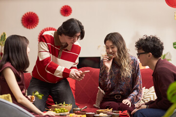 Fototapeta premium Group of Asian young adults gathering around table sharing traditional food and drinks during Tet holiday celebration, smiling and interacting with each other in festive setting