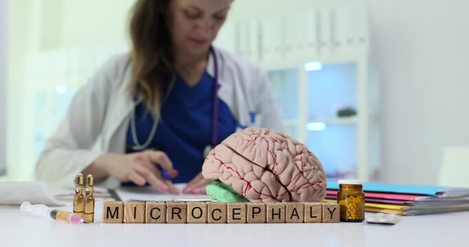 Wooden cubes form word Microcephaly near anatomical brain model indicating diagnosis of patient. Doctor carefully reviews test results at table