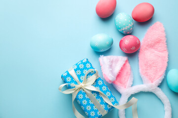 Happy Easter. Cute bunny ears, gift box and painted eggs on light blue background, flat lay. Space for text