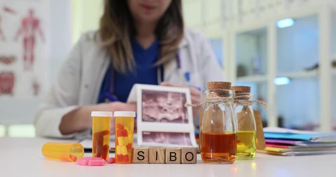 Woman doctor carefully studies ultrasound images of intestines. Wooden cubes form abbreviation SIBO clearly indicating intestinal diagnosis of patient