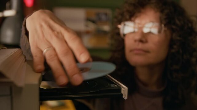 Close-up of hands and face of young Caucasian woman inserting cd-rom disk into drive on tower case, while working on retro PC computer in home study, to record file for storage