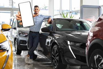 Wealthy young middle eastern man posing by brand new black sports car, showing smartphone with...