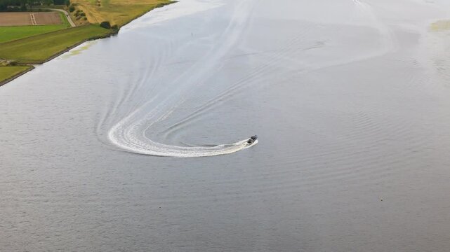 motorboat performs sharp turn river leaving curved white wake shoreline green embankments agricultural land against expansive calm water wide netherlands drone aerials nature 