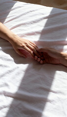 Obraz premium Tender hands of a couple touching on a white bedsheet. Vertical photo capturing a moment of love, intimacy, and connection in natural sunlight.