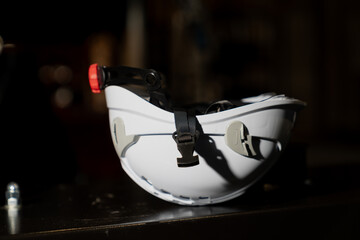 Industrial hard hat with adjustable strap and front headlamp positioned on black machinery surface...