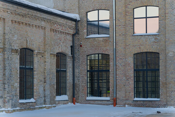 Symmetrical old factory brick buildings with grid windows and snow on ground presenting industrial heritage courtyard exterior view architecture