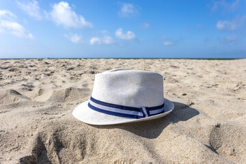 White straw hat with blue ribbon lying on sand at beach under clear blue sky. Summer vacation scene.
