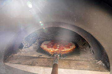 Pepperoni pizza being cooked in a traditional wood-fired oven with glowing embers