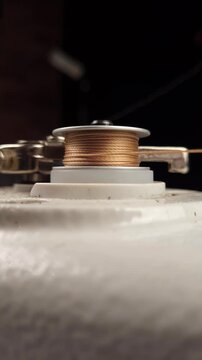 Sewing machine bobbin winder, golden thread winding onto bobbin on black background.