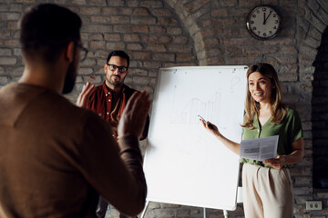 Diverse business team standing by a whiteboard in a modern office, analyzing data results and brainstorming new strategy during a corporate meeting.
