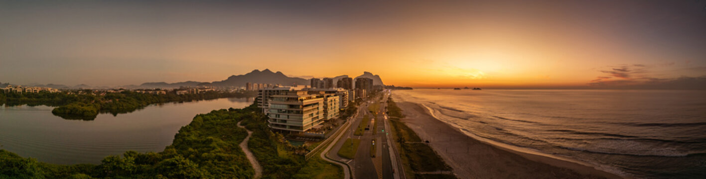 Linda imagem a&eacute;rea panoramica, mostrando o sol nascendo n praia da Barra da Tijuca, com a Lagoa da Tijuca ao lado e a Pedra da G&aacute;vea ao fundo.
