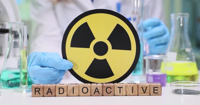 Laboratory worker raises international warning sign to indicate presence of radiation in working area. Wooden letter cubes on table form Radioactive
