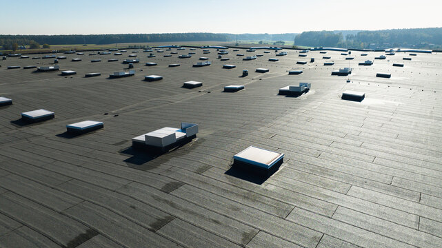 Large industrial flat roof with skylights on modern warehouse building in rural landscape