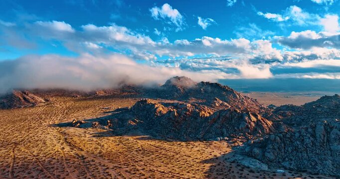 Rise over the desert covered with shrubs. Clouds spread over the rocks on sunny day. View on the amazing landscapes of Joshua Tree National Park, California, USA.