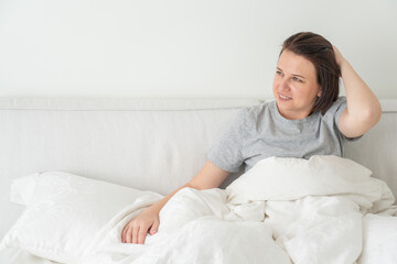 Smiling brunette woman wearing pajama sitting in bed in bedroom