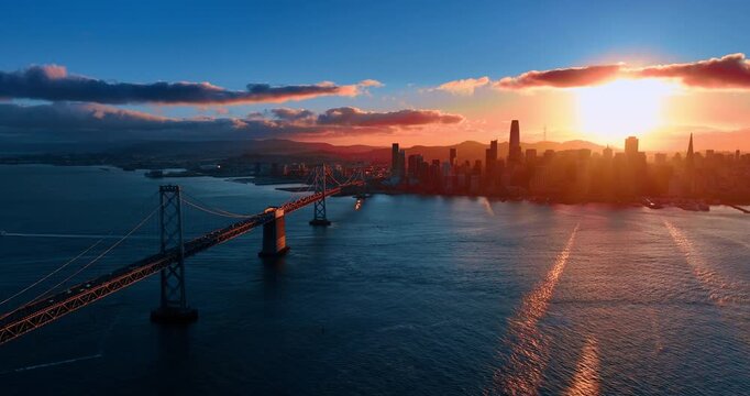 The Oakland Bay Bridge with multiple moving cars. Setting sun lights the scenery of San Francisco, California, USA. Aerial view.