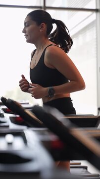 The athletic girl dressed in a black sportswear running on the treadmill. vertical video