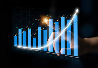 A close-up view of a hand pointing at an upward trend graph on a digital screen, illustrating financial growth and analysis in a modern office setting. Impute