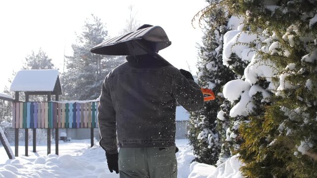 Man carrying snow shovel over his shoulder walks through a sunlit, snow covered backyard ready to clear drive and path seasonal chore, determined homeowner at work