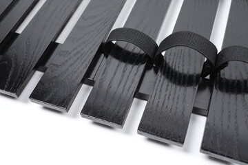 A close-up view shows a black wooden slatted structure with a visible wood grain texture, featuring integrated black fabric straps or loops designed for secure fastening of components.