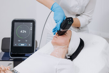 Female patient receiving RF lifting treatment at a beauty clinic, technician using a handheld device, digital display showing treatment progress, bright clinical environment © wedmoments.stock