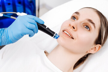 Cosmetologist performs a hydrafacial treatment on a smiling client in a skincare clinic. Concept skincare, facial treatment, beauty care