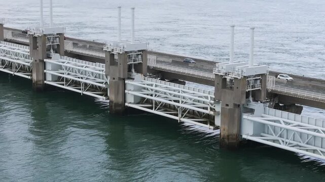 intricate white metal support trusses massive concrete piers anchor structure against shifting tidal waters focuses eastern scheldt storm surge barrier aerial shot netherlands 