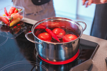 In the kitchen, there is a pot with tomatoes and chilies in boiling water.