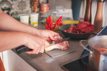 Photograph of a woman cooking in her kitchen. She is cutting chicken with a sharp knife.