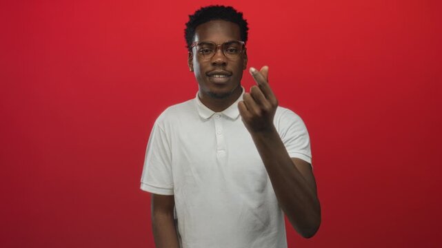 Man wearing glasses and white polo shirt making finger heart gesture in studio against red background; affection.
