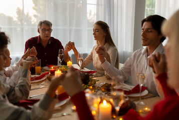 Big multi generation family holding hands and praying before festive family dinner, celebrating Christmas, sitting at table with Xmas holiday meal, expressing thanks to God at home