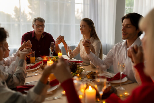 Big multi generation family holding hands and praying before festive family dinner, celebrating Christmas, sitting at table with Xmas holiday meal, expressing thanks to God at home