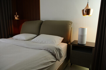 A wide-angle shot of a minimalist white air purifier placed on a bedside table in a master bedroom...