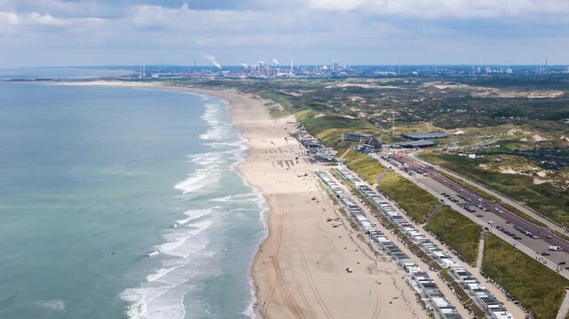 row white beach huts along sandy shore hilltop road behind industrial complex visible distant horizon zandvoort coastline high angle aerial drone view netherlands dutch coast 