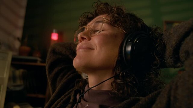 Close-up of hands and face of cheerful young 1990s woman putting on headphones, playing audio file with favorite song in mp3 player on vintage computer, while relaxing during workday