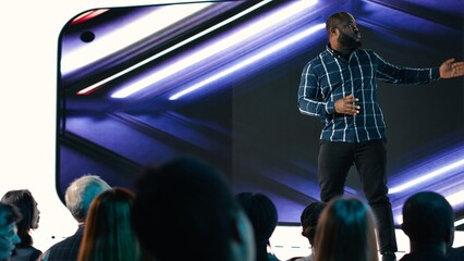 African american lead engineer revealing new smartphone launch with detailed presentation about new interface features for advertising. Launch with audience in conference hall.