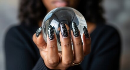 Close-up of a woman's hand with a black glitter manicure holding a crystal ball. Mystical fortune telling and future prediction concept