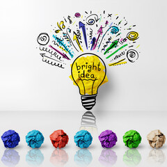 Bright idea light bulb drawn on wall with colored crumpled paper below in a creative workspace setting