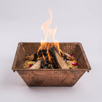 Sacred Hindu ritual fire Havan Kund with burning wood and offerings in a hammered copper pot