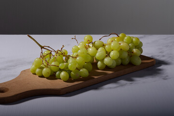 Bunch of green grapes on a wooden board in dim light.